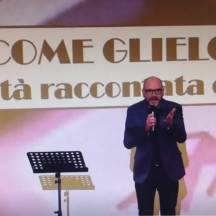 Fabrizio Palma in giacca, microfono in mano, davanti alla proiezione dello spettacolo