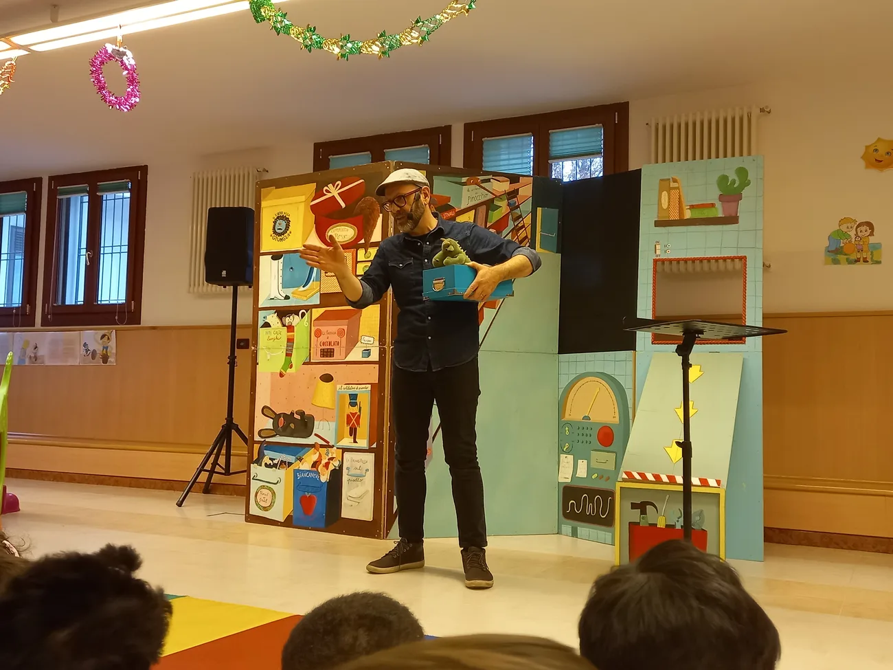 Fabrizio Palma in scena con una scatola sotto il braccio davanti alla scenografia dello spettacolo